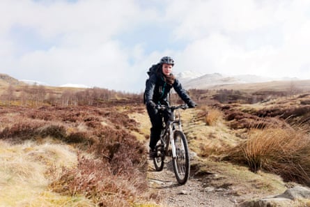 A female mountain bike rider cycling across a rugged Scottish landscape.