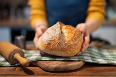 A loaf of freshly baked bread is placed on a gingham tea-towel