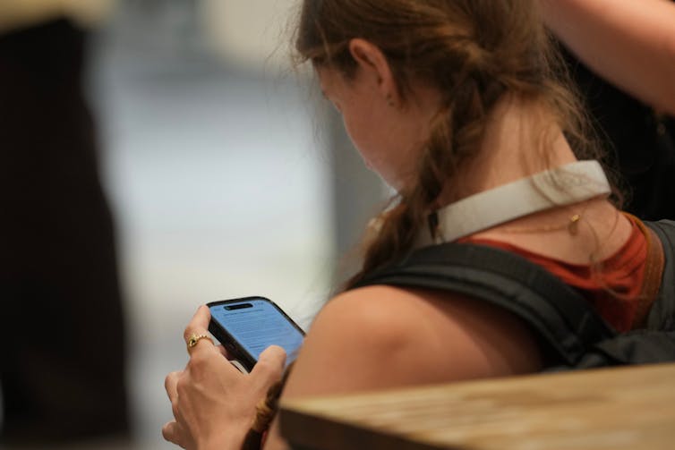 A young girl, seen from behind, looks at her cell phone