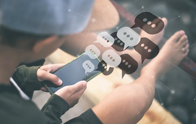 A boy looking down at a phone, with cartoonish chat icons on top of the phone.