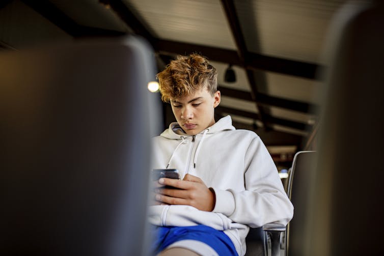 A teenage boy uses his cell phone on a school bus.