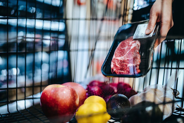 Person placing package of steak into grocery cart