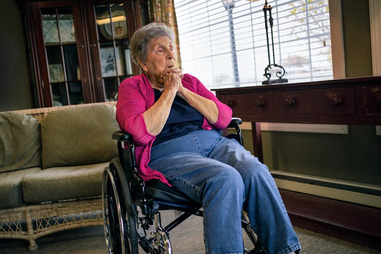 An older Hispanic woman sits in a wheelchair and stares across the room.