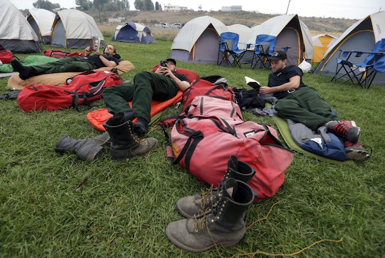 Firefighters on air mattresses with tents in the background.