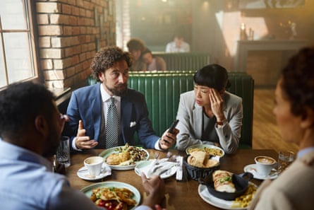 A man in a suit sits at a table talking while others listen