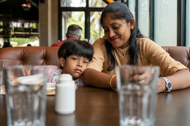 Parent smiling down at child leaning head against their arm while seated in a restaurant