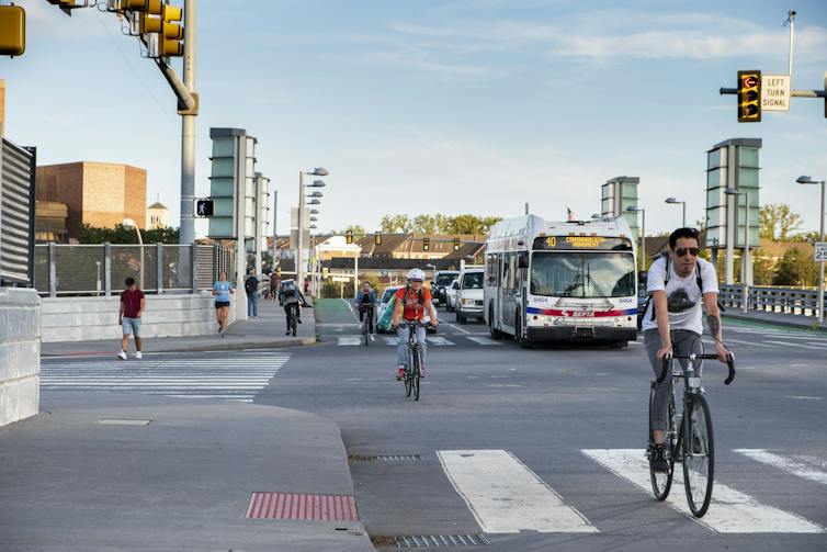 Bicyclists ride down a busy street alongside cars and a bus