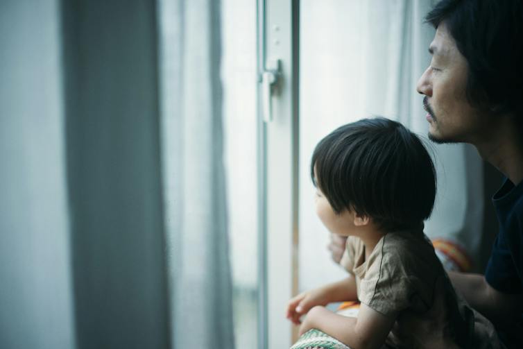 Child looking out of window with adult looking over their shoulder.