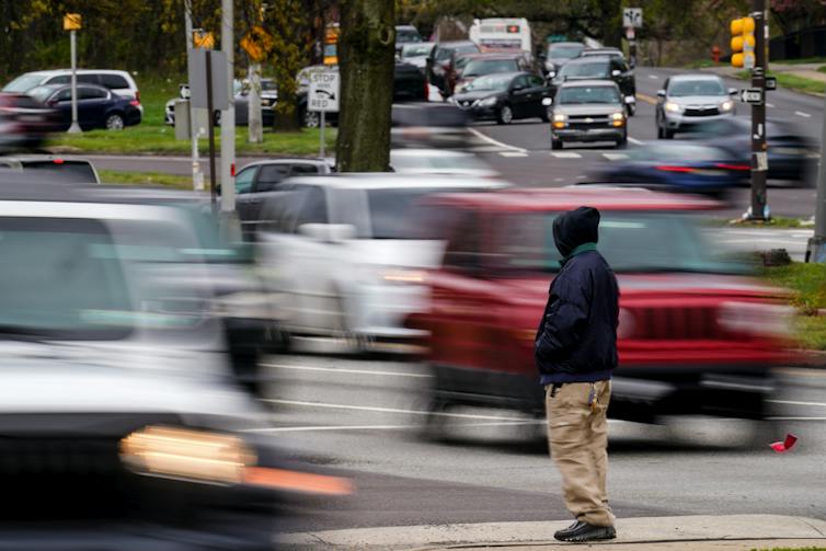 Man waits to cross a busy street filled with moving cars