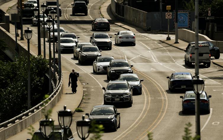 Man walks on sidewalk along traffic on an overpass