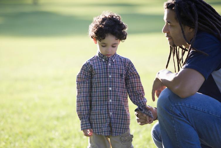 Father kneeling down holding hand of child outside