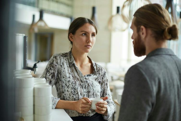 Two people having a serious conversation beside a coffee maker in an office