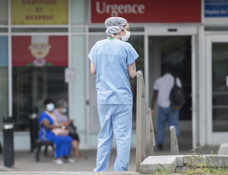 A woman in scrubs and a face maks stands outside the entrance of a hospital