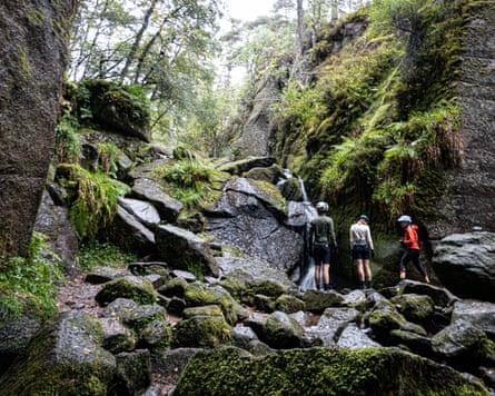 A group of people standing in a rocky area, with a waterfall in front of them