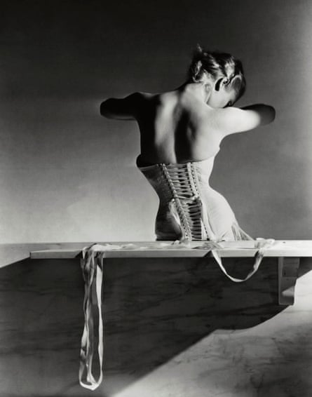 Model, seen from behind, sitting on a wooden bench, looking down through her arms, and wearing a back-lacing corset by Detolle for Mainbocher.