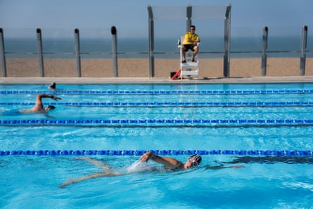 People swimming in an open-air pool with a view of the beach and sea