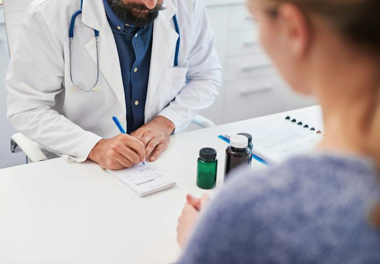 A doctor writing a prescription with a patient seen from behind
