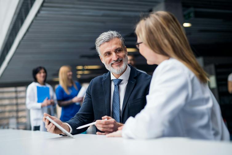 A man in a suit talking to a woman in a white coat and pointing at a device screen