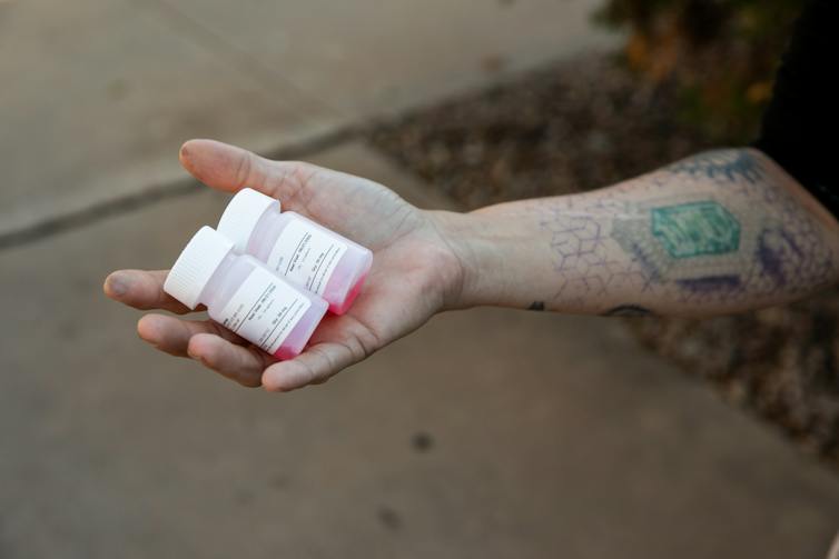Two methadone bottles filled with red liquid in the palm of an outstretched hand.