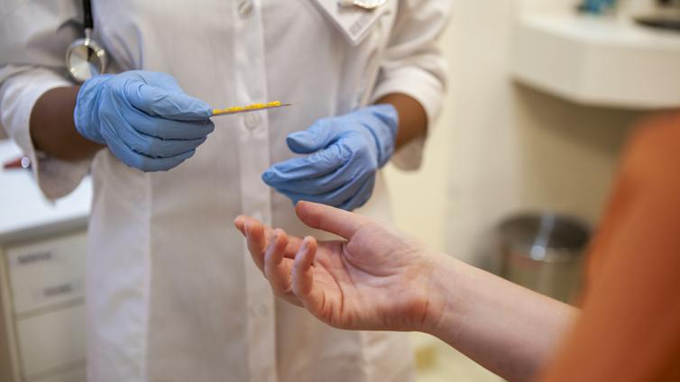 Close up shot of healthcare worker's gloved hands handing blister pack of pills to person wearing orange