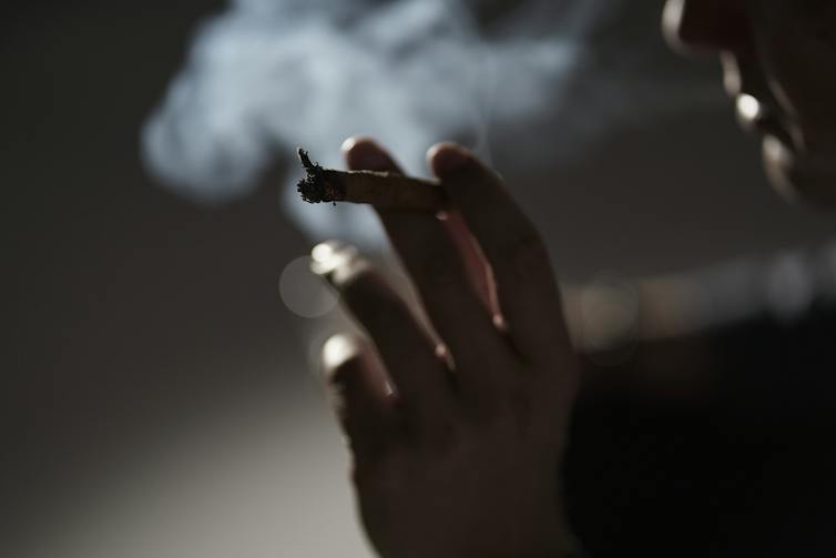 Close-up of a hand holding a cigarette, with the cigarette user exhaling smoke.