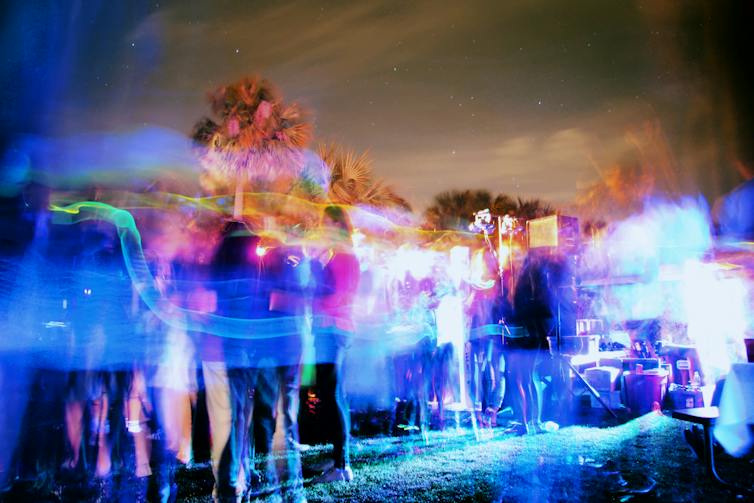 An outdoor college party with strobe lights, and palm trees in the background.