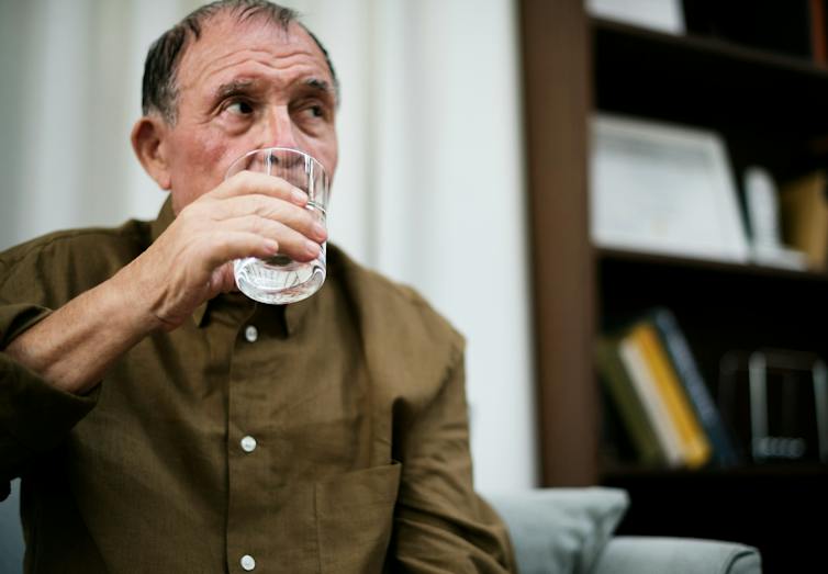 A man with grey hair drinking a glass of water