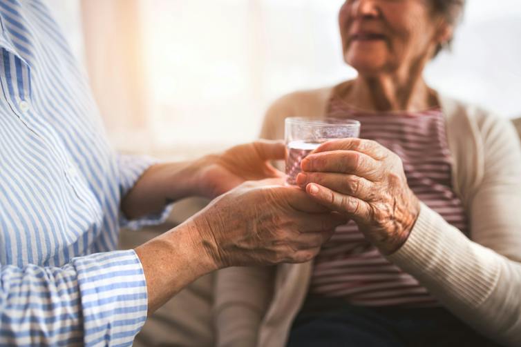 Someone handing a glass of water to an older woman slightly out of focus