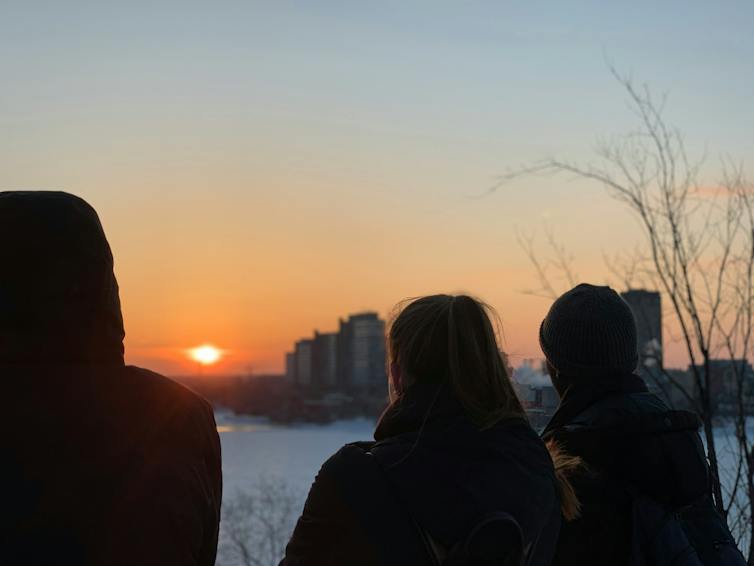 Silhouettes of young people seen against a dawn sky and snow outdoors.
